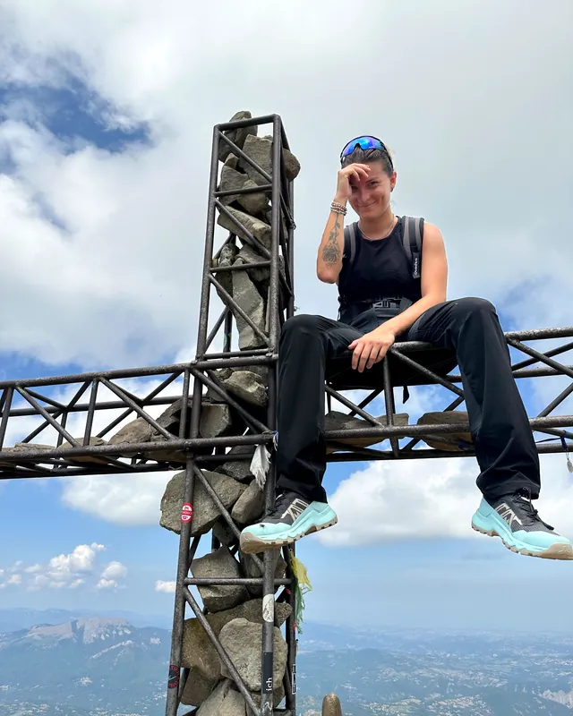 Erica seduta sulla croce di vetta di una montagna, che ride