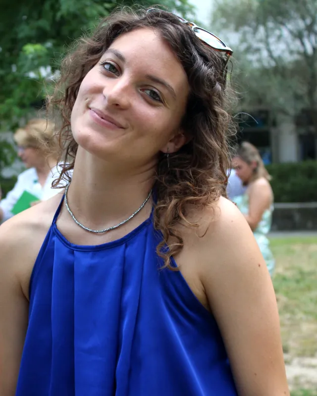 Erica con un top blu a una festa all'aperto, che sorride inclinando la testa